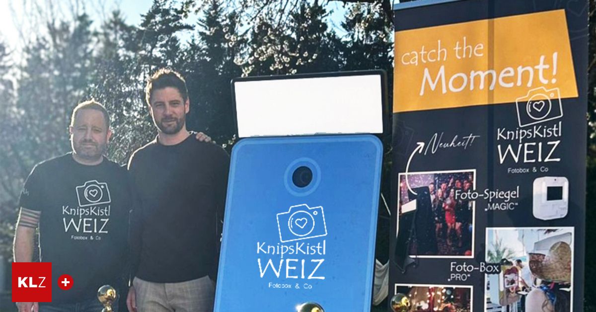 A man stands near a blue booth with the logo Knipskist WEIZ, likely a photo booth, with trees and a yellow banner in the background.