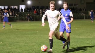 Two soccer players are in action on the field. One player is dribbling the ball, while the other is trying to steal it. The field is well-lit, and the background is blurry with people sitting in the stands.