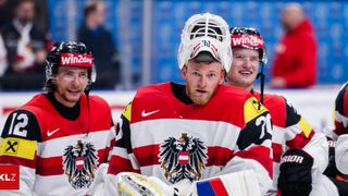 Three hockey players in red and white uniforms stand close together, wearing helmets. The player in the middle wears a white helmet with number 30.