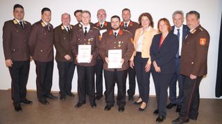 Eine Gruppe von Menschen in Uniformen, einschließlich Militäroffizieren, steht in einer Reihe. Sie halten Urkunden und posieren für ein Foto.