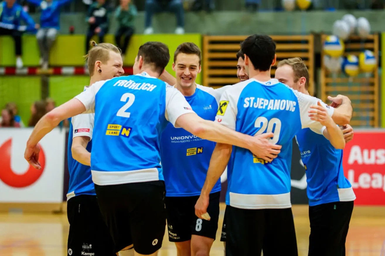 A group of basketball players in blue jerseys, with numbers 2, 8, 20, and others, celebrating a victory.