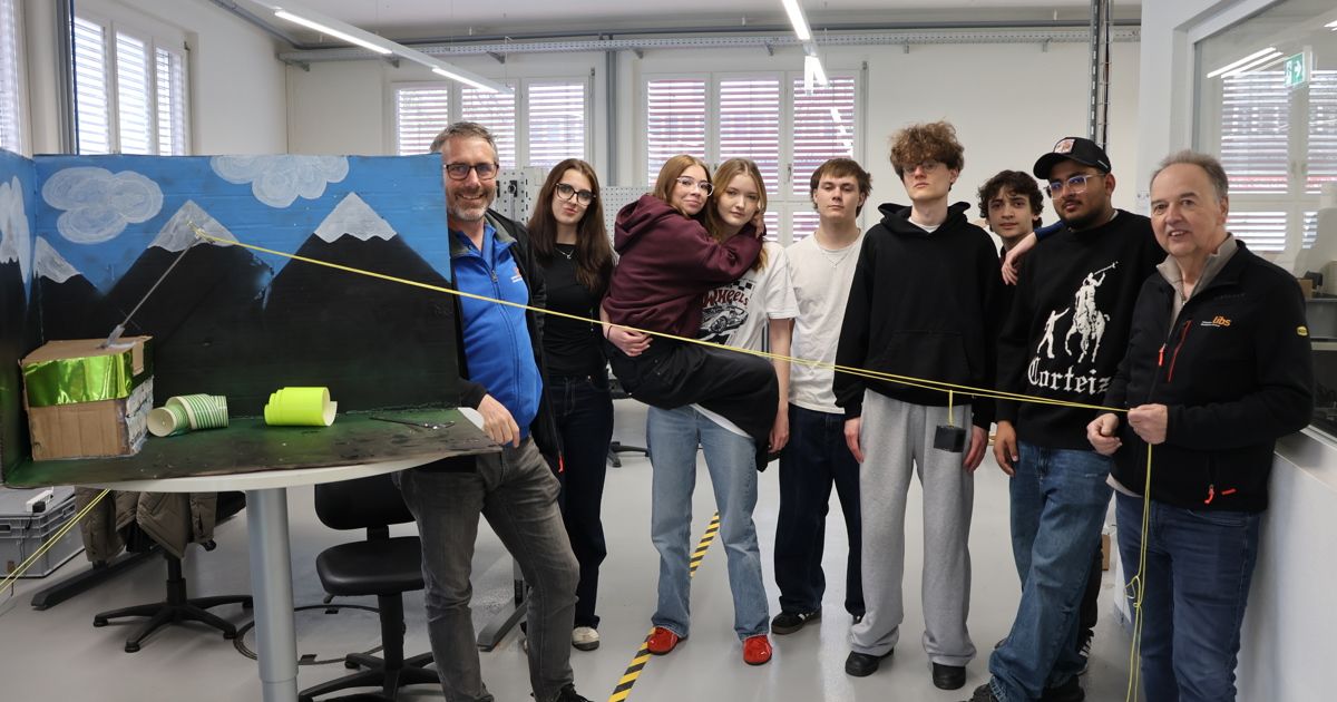 A group of students stand around a table with a large painting of a mountain, smiling and looking at the camera.