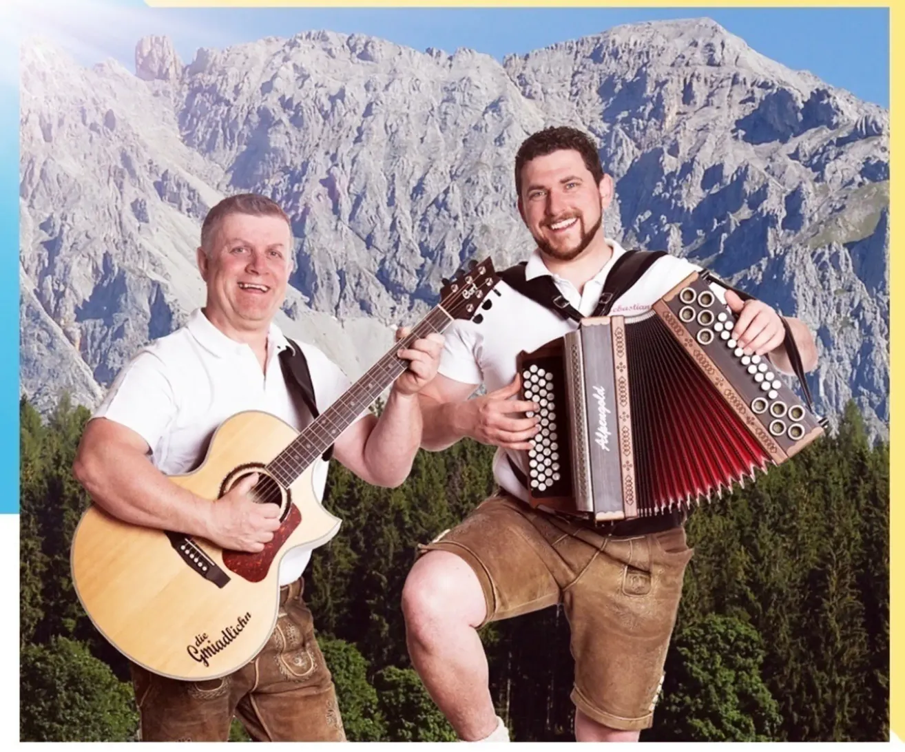 Zwei Männer stehen vor Bergen, einer mit einer Gitarre, der andere mit einem Akkordeon. Beide lächeln und sind in traditioneller Alpenkleidung gekleidet.