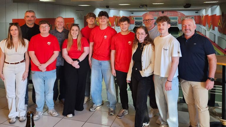A group of people wearing red shirts are standing together in a room. A woman wearing glasses is smiling and posing for a photo.