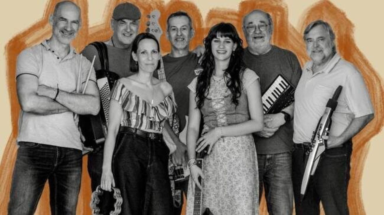 A group of musicians pose for a picture, with a man on the left playing the accordion and a man on the right holding a keyboard.