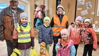Eine Gruppe von Kindern und einem Erwachsenen stehen in einem Flur, alle in Winterkleidung gekleidet und halten Tüten. Der Erwachsene lächelt und die Kinder posieren für ein Foto.