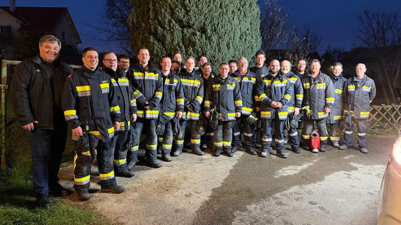 A group of firefighters in uniform standing outside at night. They are smiling and posing for a photo.