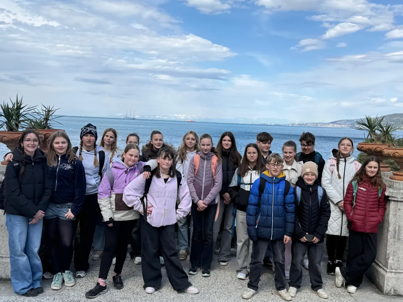 A group of young people are posing for a photo in front of the ocean on a sunny day.