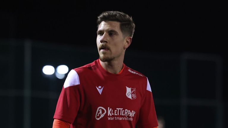 Ein Fußballspieler in einem roten Trikot mit KLETTERPARK steht unter einem dunklen Nachthimmel und schaut nach links.