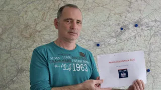 Ein Mann in einem türkisen T-Shirt hält ein weißes Papier mit dem Text 'Kriminalitätsstatistik 2025' vor einem Kartenhintergrund.