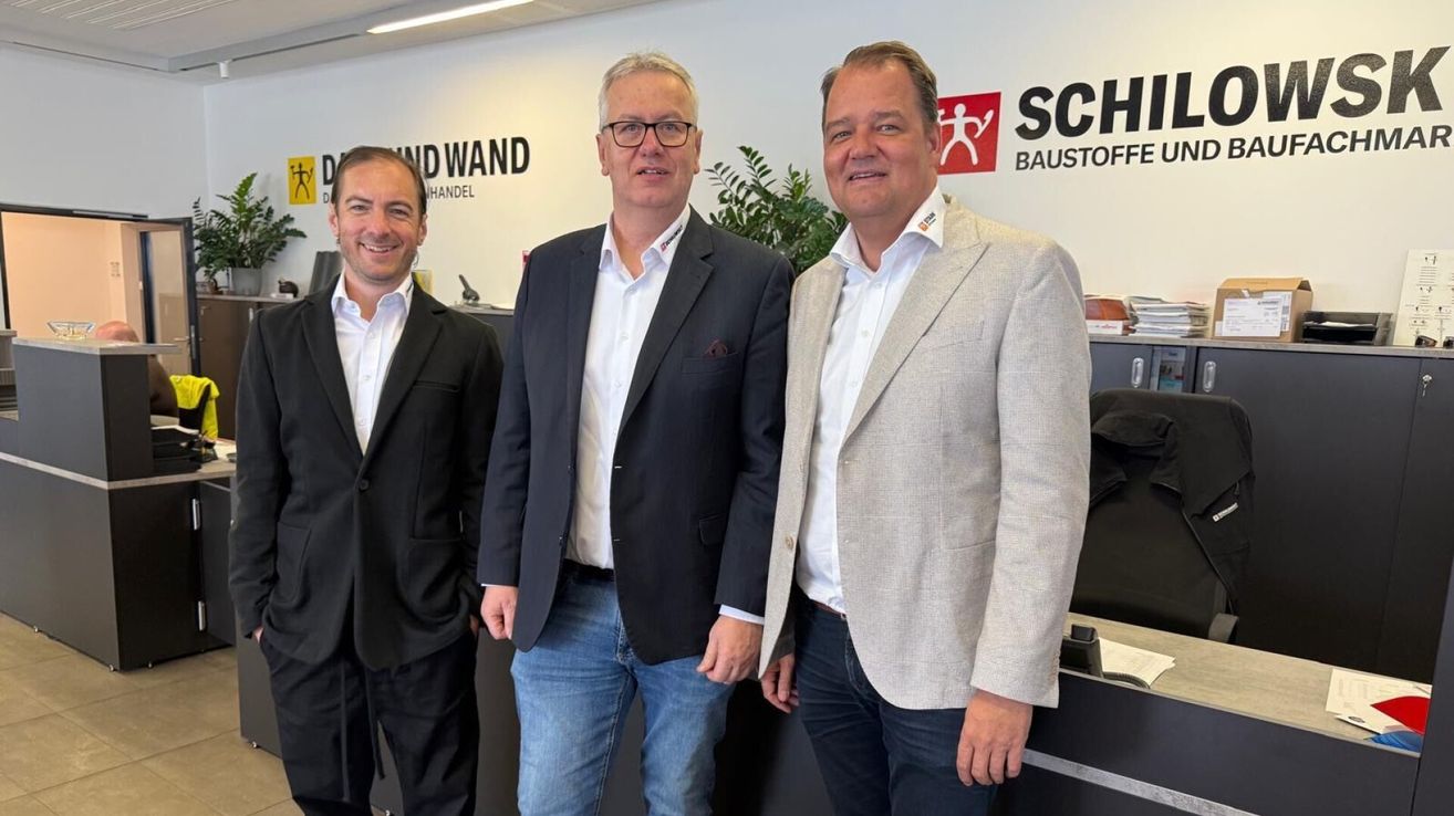 Three men in suits stand next to each other in front of a SCH logo. They are smiling and seem to be posing for a photo.