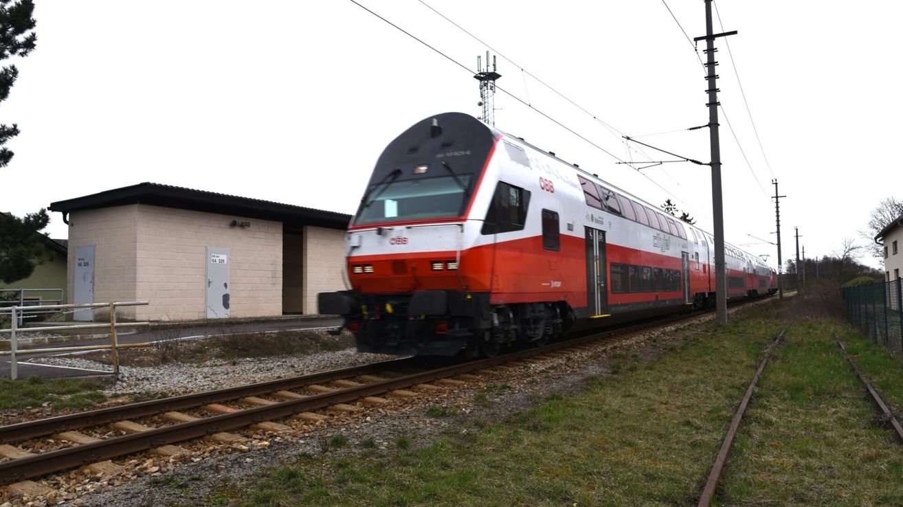 Ein roter und weißer Zug mit der Nummer '088' fährt auf den Gleisen, hinter ihm ein Gebäude.