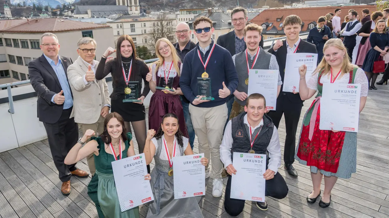 Group photo of young people with medals and certificates on a rooftop terrace. Buildings in the background.