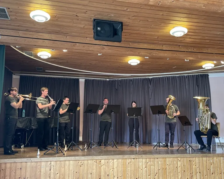 A group of musicians are performing on stage. They are playing various instruments. The stage is lit by spotlights. The audience is not visible.