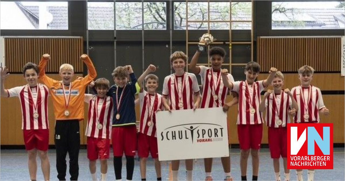 A group of young athletes are celebrating their victory with medals and a trophy in a gym. They are wearing red and white uniforms.