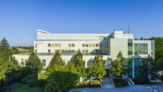 Ein großes Gebäude mit mehreren Fenstern, umgeben von Bäumen, unter einem klaren blauen Himmel.