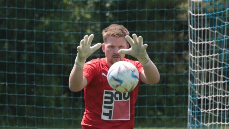 Ein Mann mit roten und weißen Handschuhen übt Fußball vor einem Netz.