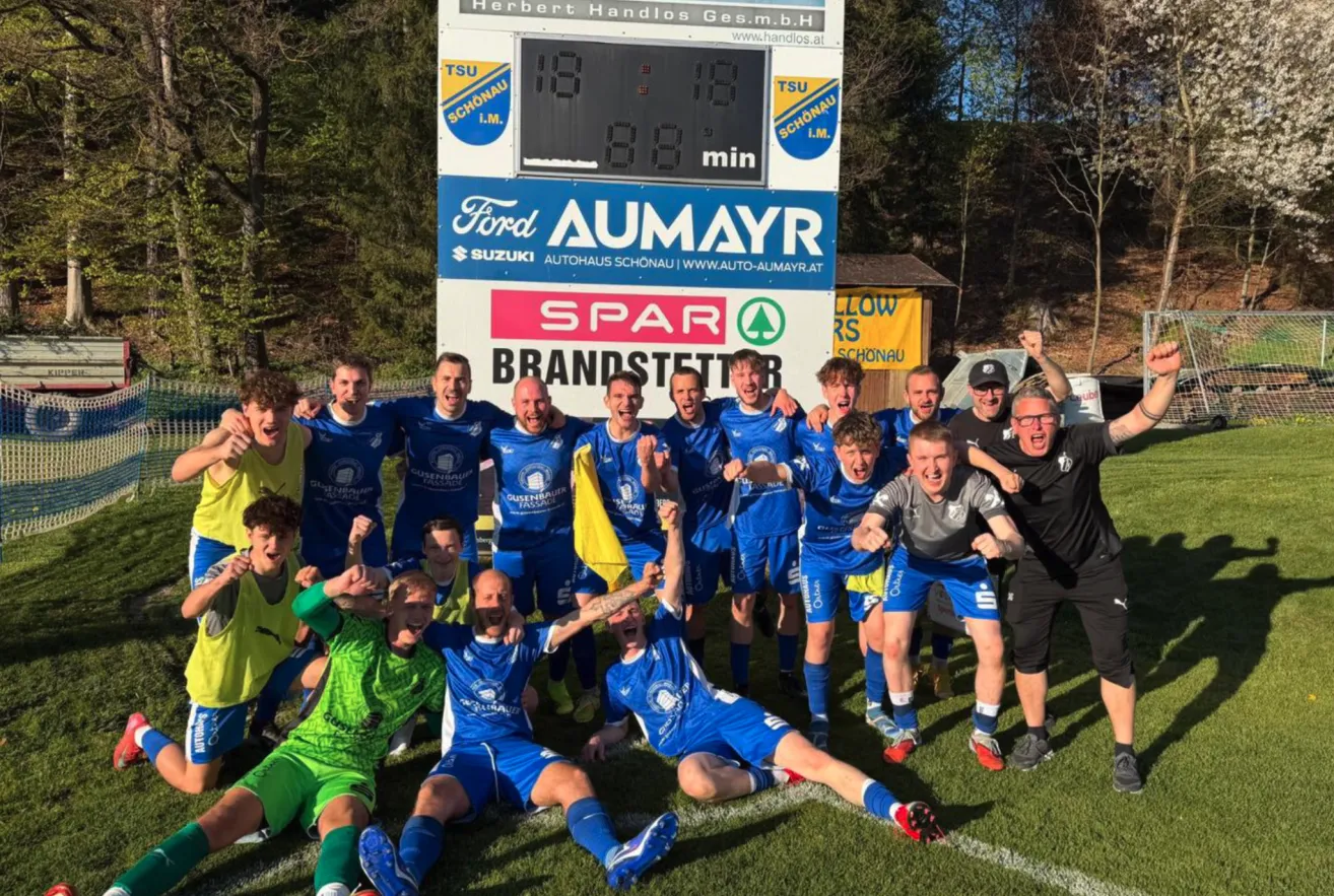 Eine Fußballmannschaft in blauen Trikots feiert den Sieg mit einem Spielstand von 18-18. Sie posieren für ein Foto auf dem Spielfeld.