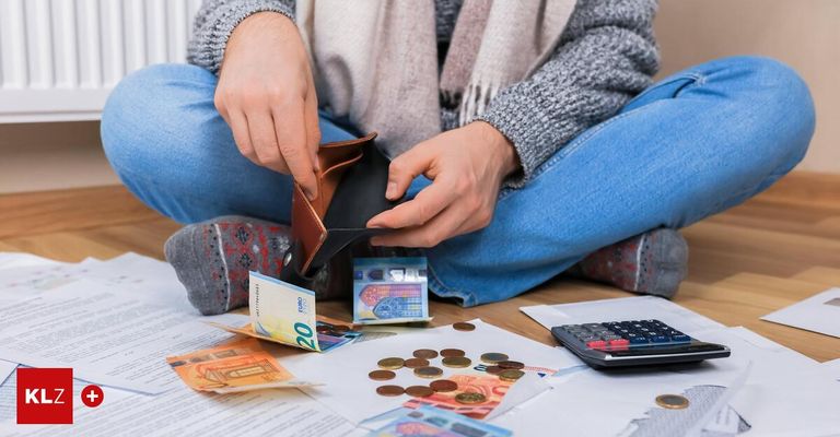 Eine Person überprüft ihre Brieftasche, umgeben von Geldscheinen und Münzen auf einem Tisch mit einem Taschenrechner.