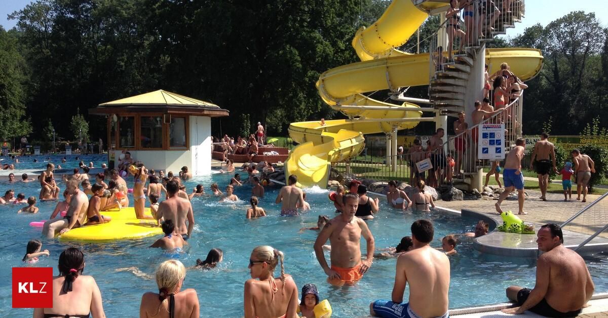Menschen schwimmen im Pool und genießen die gelbe Wasserrutsche. Ein Gebäude mit gelbem Dach steht in der Nähe des Pools. Einige Leute sitzen auf den Stufen der Wasserrutsche.