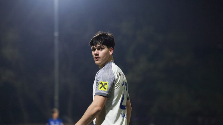 Ein junger männlicher Fußballspieler in einem Trikot mit gelbem X-Logo, das auf einem Feld steht.