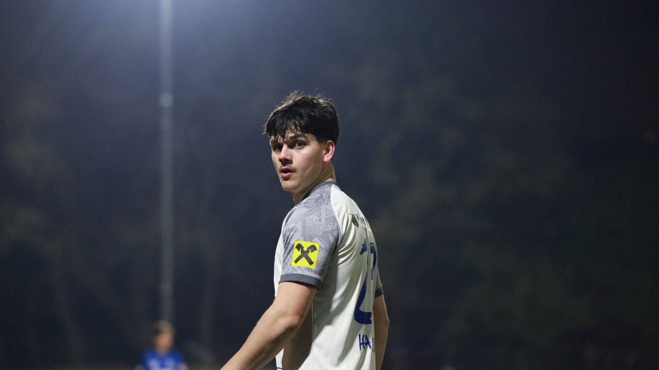Ein junger männlicher Fußballspieler in einem Trikot mit gelbem X-Logo, das auf einem Feld steht.