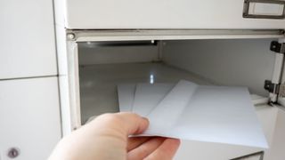 Eine Hand öffnet eine Schublade, um zwei gefaltete Papiere darin zu zeigen. Die Schublade ist weiß und Teil eines größeren weißen Schranks.