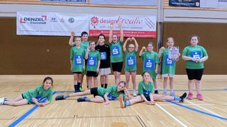 Eine Gruppe junger Menschen in grünen Shirts und Shorts posiert für ein Foto in einer Sporthalle. Einige stehen, andere sitzen und ein Mädchen hält eine Urkunde.