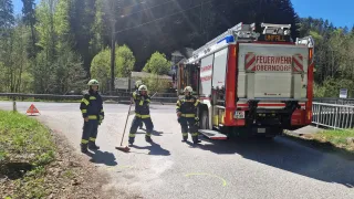 Feuerwehrleute in voller Montur markieren einen Kreis auf der Straße mit einem Besen. Der Feuerwehrwagen ist hinter ihnen geparkt.