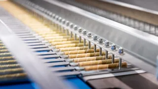 Eine Produktionslinie mit Reihen zylindrischer Objekte, die verarbeitet werden, von Metallklemmen gehalten und sich durch eine metallische Anordnung bewegen.