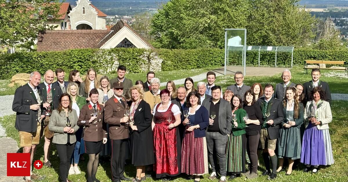 Eine Gruppe von Menschen in traditioneller Kleidung posiert für ein Foto in einer malerischen Außenumgebung, mit Gebäuden und Grün im Hintergrund.
