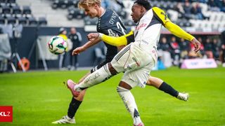 Zwei Fußballspieler, einer in Gelb und einer in Schwarz, konkurrieren auf dem Spielfeld um den Ball.