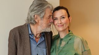Ein älterer Mann mit grauem Haar und Bart steht neben einer Frau mit kurzen Haaren, beide lächeln und schauen sich an.