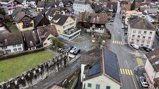 Luftaufnahme einer Kleinstadt mit mehreren Häusern, einige mit Solarpanelen auf den Dächern. Autos sind auf der Straße und dem Bürgersteig geparkt.