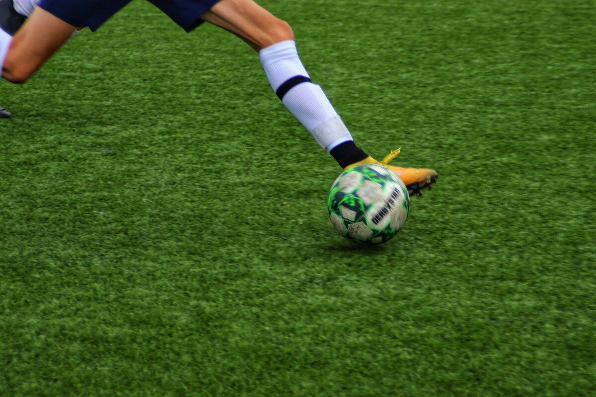 Ein Fußballspieler in blauer und weißer Uniform tritt einen grün-weißen Fußball.