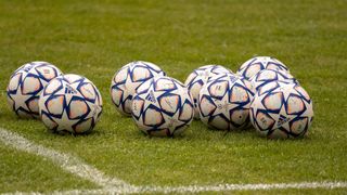 Mehrere Adidas-Fußballbälle mit blauen und weißen Sternen liegen auf einem grünen Feld neben einer weißen Linie.