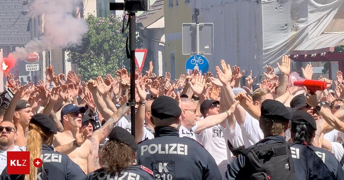 Eine Menschenmenge, teilweise ohne Oberkörperbekleidung, erhebt ihre Hände und schreit. Polizeibeamte mit dem Wort 'POLIZEI' auf ihren Uniformen sind darunter.