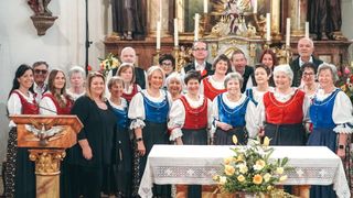 Eine Gruppe von Menschen in traditioneller Kleidung posiert für ein Foto vor einem Altar mit Blumen, Kerzen und einer Statue.