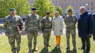 Fünf Personen in Uniform, darunter eine Frau, stehen auf einem Rasenfeld mit einem Gebäude im Hintergrund.