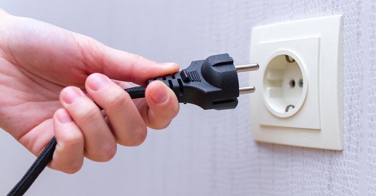 Eine Hand steckt einen schwarzen Netzstecker in eine weiße Wandsteckdose.