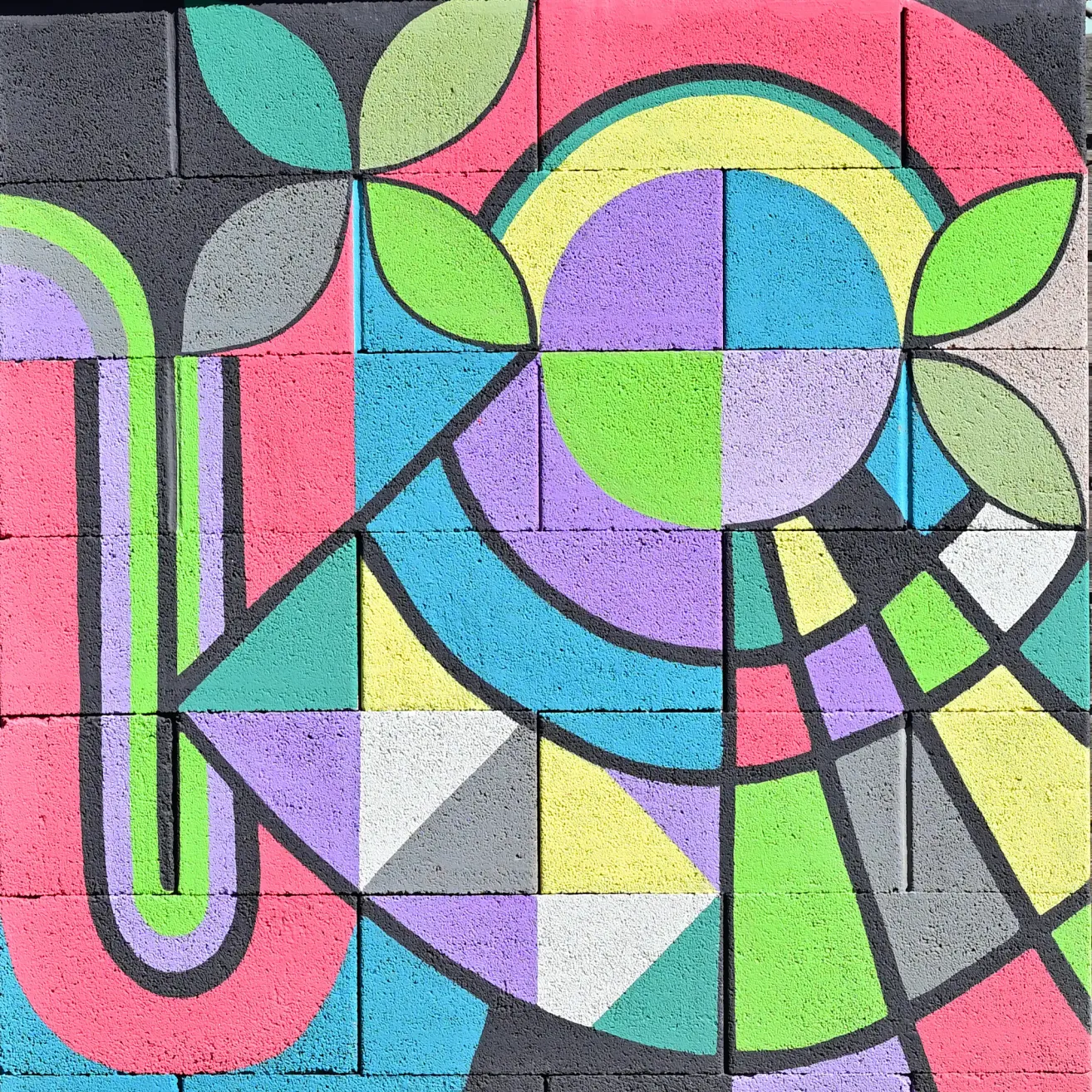Ein lebendiges, abstraktes Wandbild mit einem Buchstaben U in kräftigen Farben und einem zentralen Blumenmuster aus Quadraten und Bögen.