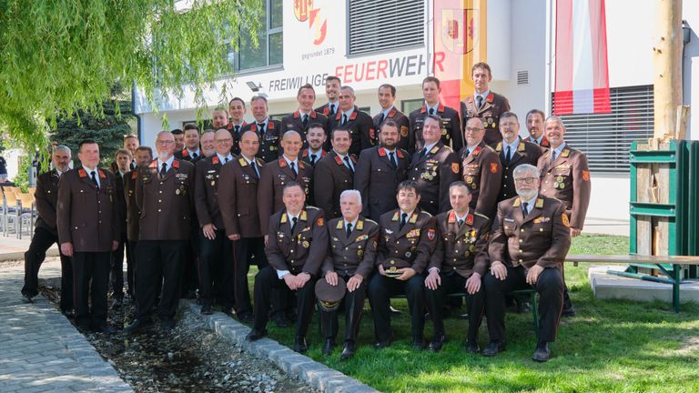 A group of uniformed individuals, likely firefighters, are posing for a photograph in front of a building with a sign reading 'Freiwillige Feuerwehr'.