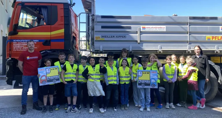 Eine Gruppe von Kindern in Sicherheitswesten posiert für ein Foto vor Lastwagen. Sie halten Schilder mit der Aufschrift LKW und FREUNDE auf der Straße.
