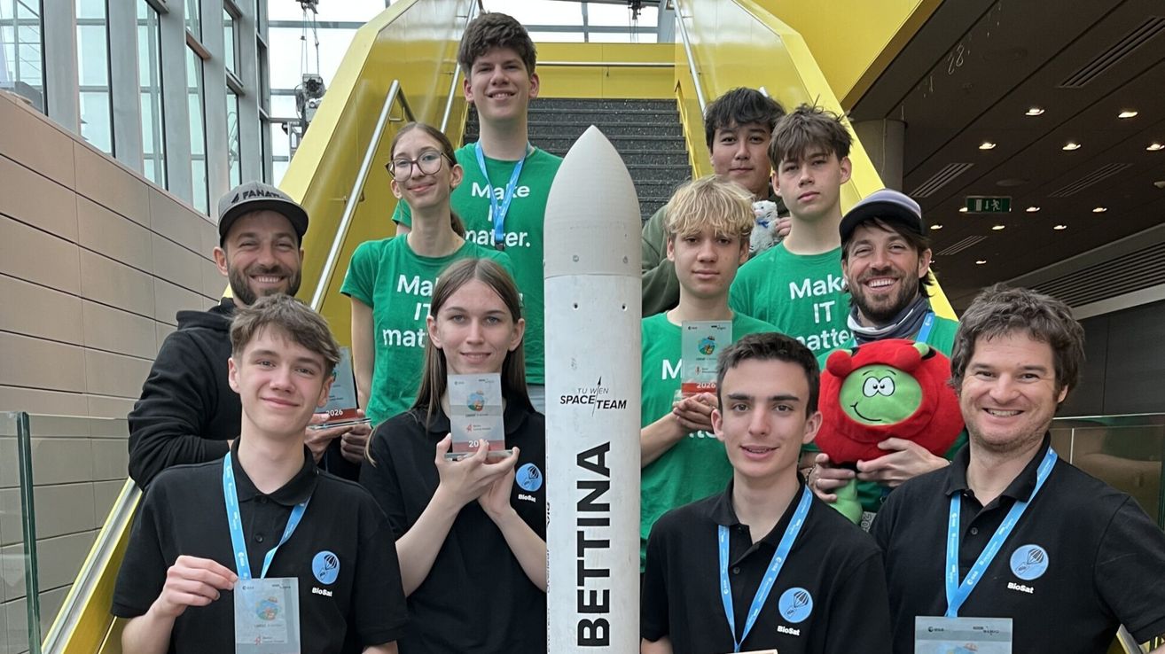 Eine Gruppe junger Leute in grünen und schwarzen T-Shirts posiert mit einer weißen Rakete mit der Aufschrift BETTINA. Sie lächeln und halten Auszeichnungen, ein Mann hält ein rotes Kuscheltier.