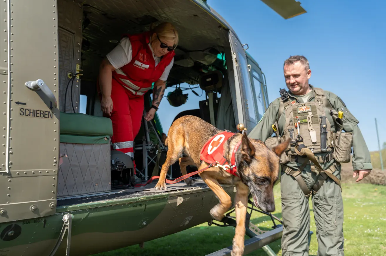Eine Frau in Rot hilft einem Hund mit rotem Halsband mit einem Kreuz, einen Militärhubschrauber zu betreten.