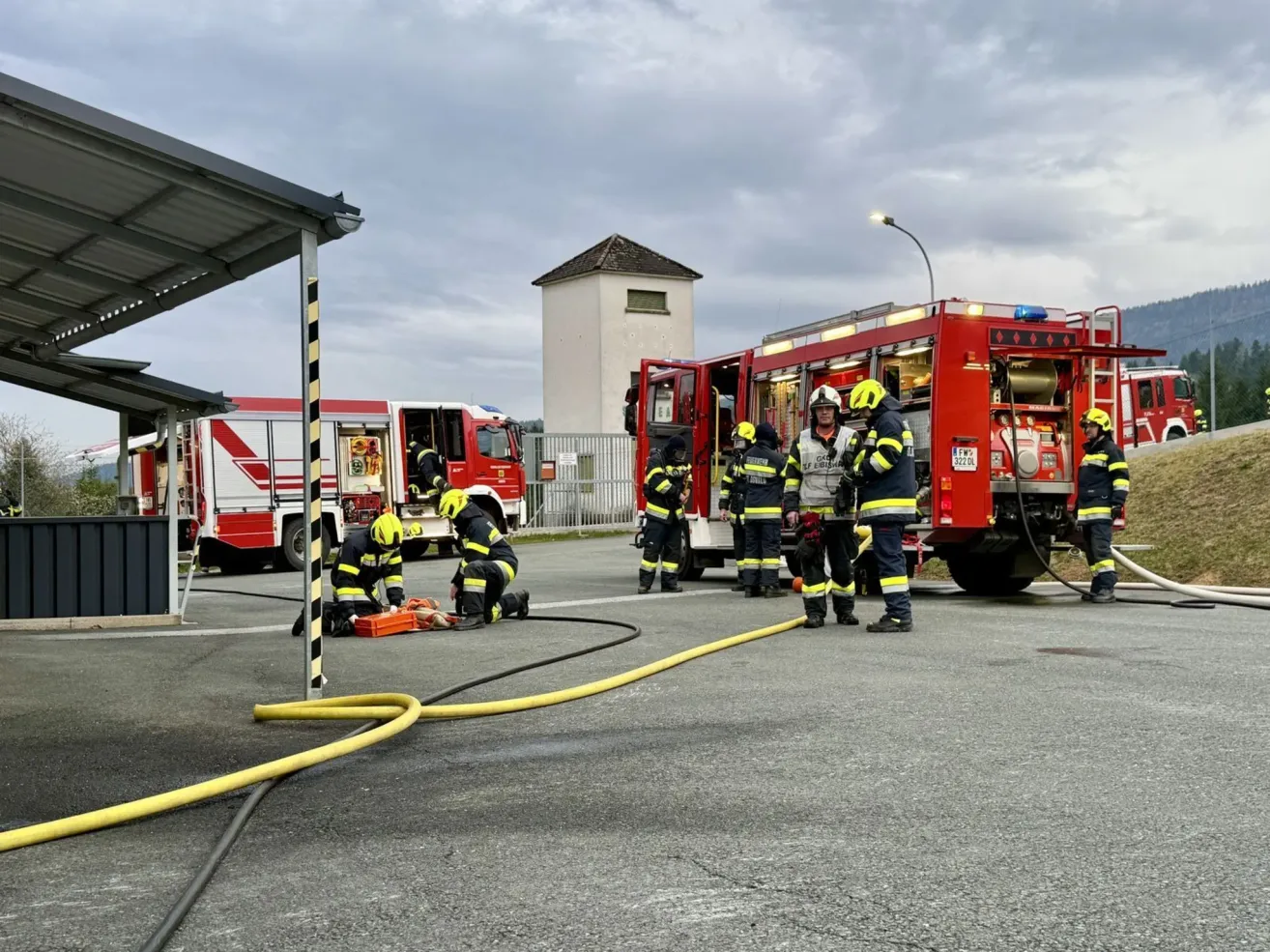 Feuerwehrleute arbeiten an einem Feuerwehrauto mit gelben Schläuchen auf der Straße. Sie bereiten sich auf einen möglichen Brandeinsatz vor.