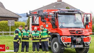 Vier Feuerwehrleute stehen vor einem roten Feuerwehrauto mit angekoppeltem Drohnen. Sie tragen alle grüne Westen und halten elektronische Geräte.