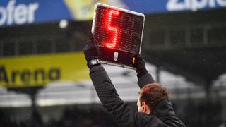 Ein Mann hält ein Anzeigebrett mit der Nummer 5 in einem Sportstadion an einem regnerischen Tag.