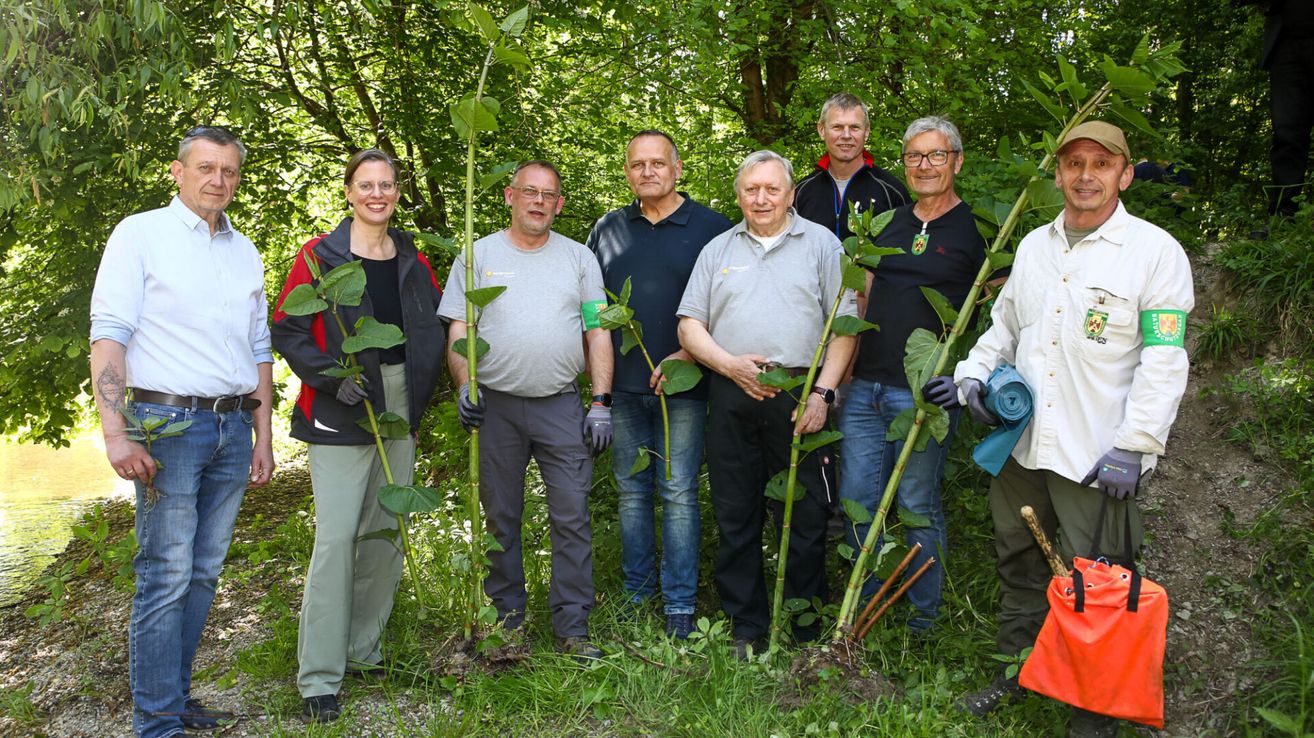 Eine Gruppe von Menschen steht in einem Garten mit Pflanzen und lächelt für ein Foto. Sie sind von grünen Bäumen und Büschen umgeben.