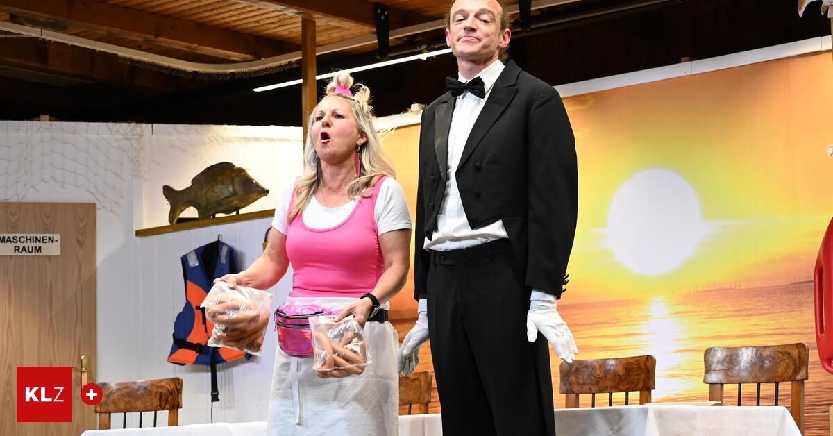 Eine Frau in einem rosa Oberteil und einer weißen Schürze hält Plastiktüten in der Hand und steht neben einem Mann in formaler Kleidung. Hinter ihnen befindet sich eine Bühnenkulisse mit Sonnenuntergang und einem Fisch.